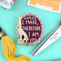 Decorative button with text 'I make, therefore I am' on a colorful background with yarn and knitting needles.