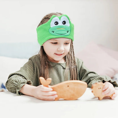 Child wearing a green frog eye mask while holding wooden toys. JOEYZ_soft_headphones_frog_dino