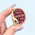Person holding a red enamel pin with a giraffe design and text on a white background
