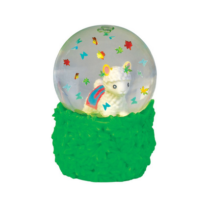 A decorative snow globe figurine with a white llama or alpaca inside a clear globe, surrounded by small colorful star and butterfly decorations, set on a textured bright green base against a plain white background. Smooshos_alpaca_snow_dome_squishiy_close_up