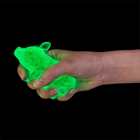 Hand holding a green glowing pig
-shaped object against a black background. Smooshos_super_squeeze_pigs_glow
