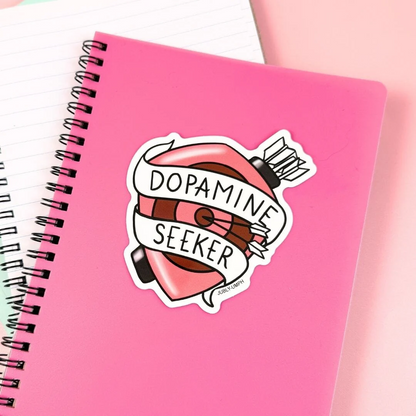 Pink notebook with a 'Dopamine Seeker' sticker on a white background. Sticker_Jubly_Umph_Dopamine_on_book