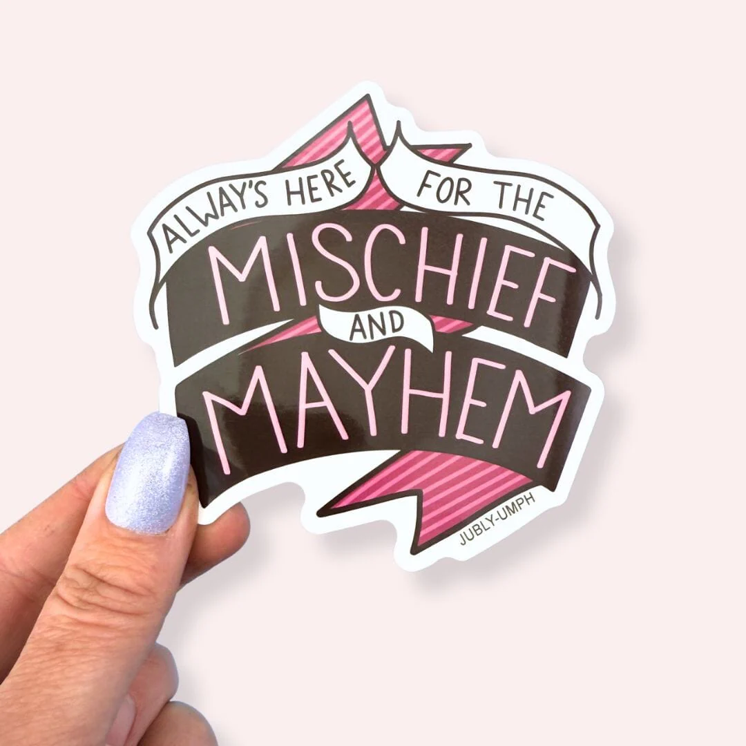 Sticker with text 'Always here for the mischief and mayhem' held by a hand on a light pink background. Sticker_Jubly_Umph_always_here_for_the_mayhem