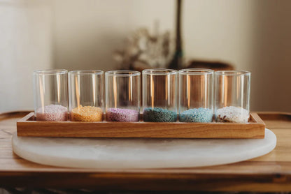Set of six small glass containers with colorful sand on a wooden tray