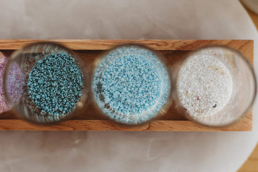 Three glass containers with colorful sand in a wooden holder on a marble surface