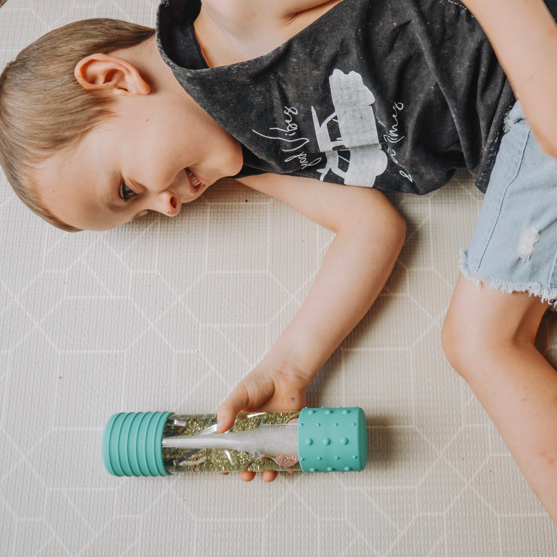 Boy_lying_on_floor_smiling_and_watching_Jelly_Stone_designs_DIY_Calm_Down_bottles_mint